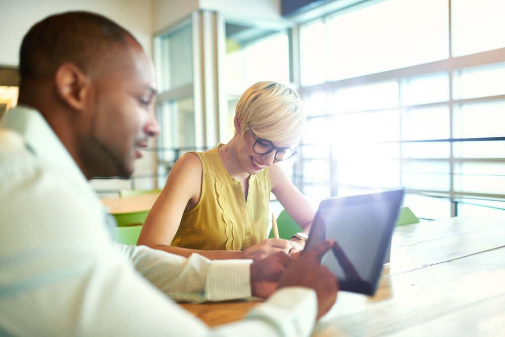 Two creative millenial small business owners working on social media strategy using a digital tablet while sitting at desk (1)